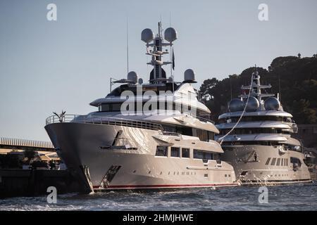 Zwei riesige Yachten befinden sich im Hafen von Monaco bei Sonnenuntergang, Sonnenreflexe sind auf glänzenden Brettern von Motorbooten, der verchromte Handlauf, Megayacht ist vertäut Stockfoto