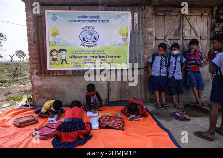 Eine Grundschule an der Grenze zwischen Indien und Bangladesch wird auf einer leeren Straße neben dem Zaun in Nabin Nagar, Westbengalen, abgehalten. Die Regierung des Bundesstaates Westbengalen hat ‘Paray Shikshalaya’ ins Leben gerufen, ein Schulprogramm, das sich an Grundschüler richtet, die in den letzten zwei Jahren aufgrund der Schließung von Schulen aufgrund von Covid-19 aus dem formalen Bildungssystem ausgefallen sind. Indien. Stockfoto