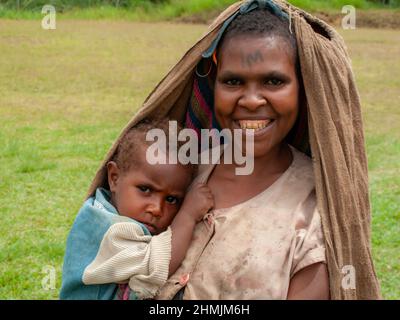 Mutter und Kind in den Bergen der Eastern Highland Province, Papua-Neuguinea. Mutter lächelt und hat eine Tätowierung auf ihrer Stirn. Stockfoto