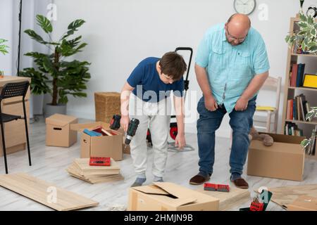 Ein Vater und ein Sohn machen sich daran, ein Bücherregal zusammenzustellen. Stockfoto