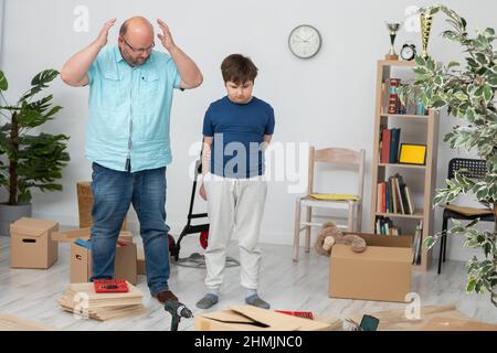 Der Vater legt seine Hände hoch und der Sohn schaut auf das Chaos im Zimmer. Stockfoto