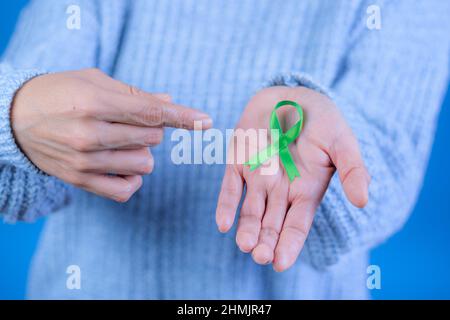 Grünes Band zur Unterstützung des Bewusstseins für Leber- und Nebennierenkrebs, menschliche Hände halten grünes Band. Weltkrebstag. Platz für Text Stockfoto