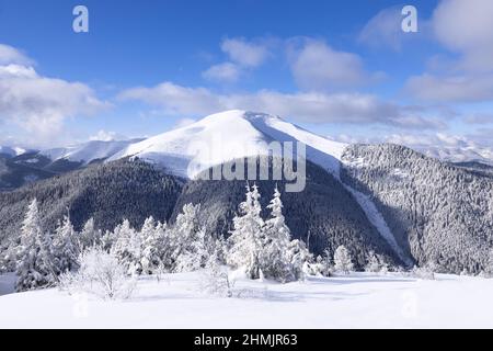 Natur Winterlandschaft. Auf dem mit Schnee bedeckten Rasen führt ein ausgetretene Pfad zum hohen Berg mit schneeweißem Gipfel. Schneebedeckter Hintergrund. Lo Stockfoto