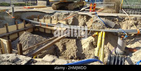 Der Prozess der Verlegung von Engineering- und Heizsystemen. Viele mehrfarbige Kunststoffrohre befinden sich in einem Sandgraben in der Perspektive Stockfoto