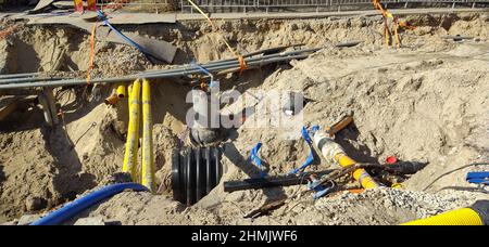 Der Prozess der Verlegung von Engineering- und Heizsystemen. Viele mehrfarbige Kunststoffrohre befinden sich in einem Sandgraben in der Perspektive Stockfoto