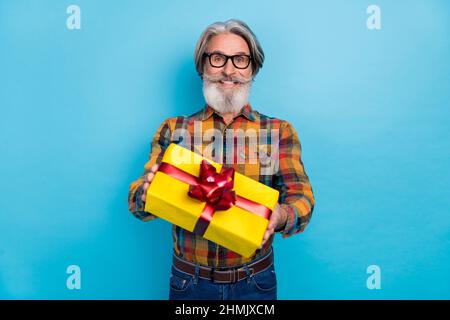 Foto von ziemlich aufgeregt pensionierten Mann tragen karierte Hemd Brille geben Ihnen Geschenk-Box isoliert blauen Hintergrund Stockfoto