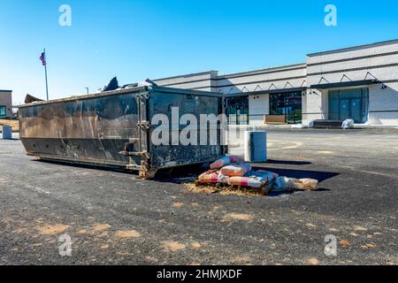 Horizontale Aufnahme eines tragbaren Müllhalters oder Müllwagens vor einer kommerziellen Baustelle. Stockfoto