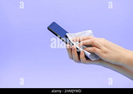 Die Hände der Frauen wischen ein Mobiltelefon mit einem weichen Tuch ab. Antiseptische Behandlung des Telefons. Stockfoto