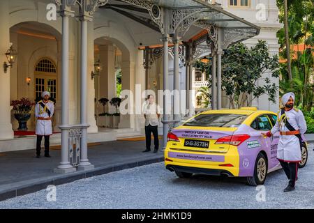 Singapur - 08. September 2019: Sikh-Türsteher in Militäruniform hilft einem Kunden aus dem Taxi im legendären Raffles Hotel Stockfoto