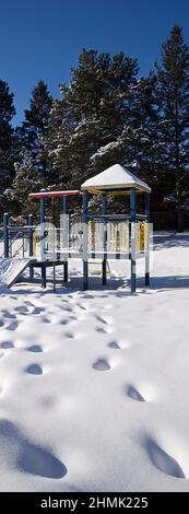 Panorama-Vertikalfoto der Rutsche - Ausrüstung des Spielbereichs für Kinder, die mit Schnee bedeckt ist, mit Fußabdruck im öffentlichen Park. Vertikales Format Hintergrund pho Stockfoto