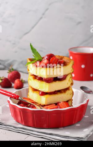 Quark-Auflauf in roter Keramikform, mit Erdbeeren auf grauem Hintergrund verziert, Nahaufnahme Stockfoto