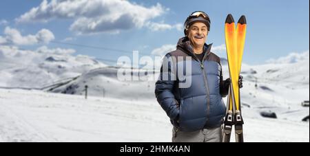 Reifer Mann lächelt und hält ein Paar Ski auf einem Berg Stockfoto