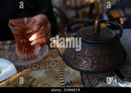 Verschwommene aserbaidschanische Frau trinkt traditionellen Tee mit Metall-Teekannen Stockfoto