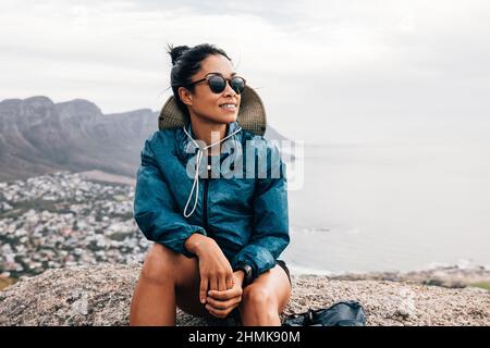 Die junge Wanderin genießt die Aussicht, während sie auf einem Berg sitzt Stockfoto
