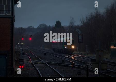 London midland Bombardier Klasse 172 mit seinen Scheinwerfern auf der Strecke und roten Signalen an der Kreuzung Stourbridge in einer dunklen, nassen Nacht Stockfoto