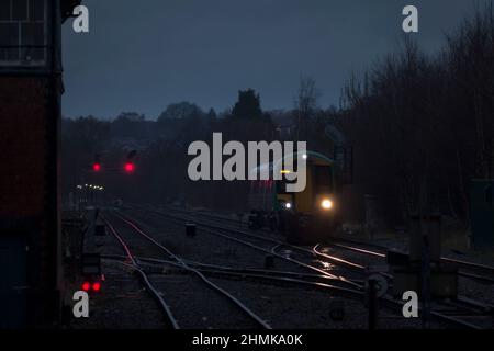 London midland Bombardier Klasse 172 mit seinen Scheinwerfern auf der Strecke und roten Signalen an der Kreuzung Stourbridge in einer dunklen, nassen Nacht Stockfoto