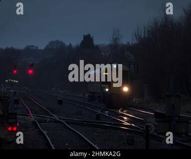 London midland Bombardier Klasse 172 mit seinen Scheinwerfern auf der Strecke und roten Signalen an der Kreuzung Stourbridge in einer dunklen, nassen Nacht Stockfoto