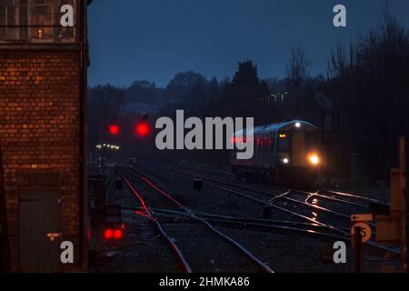 London midland Bombardier Klasse 172 mit seinen Scheinwerfern auf der Strecke und roten Signalen an der Kreuzung Stourbridge in einer dunklen, nassen Nacht Stockfoto