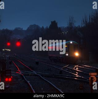 London midland Bombardier Klasse 172 mit seinen Scheinwerfern auf der Strecke und roten Signalen an der Kreuzung Stourbridge in einer dunklen, nassen Nacht Stockfoto