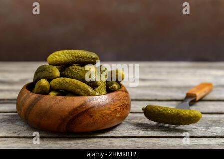 Schüssel mit eingelegten Gurken und Gabel mit Gurke auf einem rustikalen Holztisch. Stockfoto