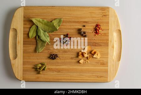 Ein Set Gewürze zum Kochen. Lorbeerblatt, trockener Knoblauch, eine Mischung aus Paprika, Oregano und Chili liegen auf einem Küchenbrett aus Holz. Draufsicht. Stockfoto