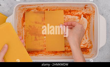 Frau, die Tannen-Nudeln auf den Boden der Backform legt. Rezept für Spinat-Lasagne Stockfoto