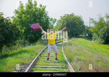 Ein fröhlicher Mann mit einem roten Koffer springt auf der Eisenbahn Stockfoto