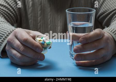 Ein Mann sitzt an einem Tisch und hält ein Glas Wasser und Pillen in den Händen. Stockfoto