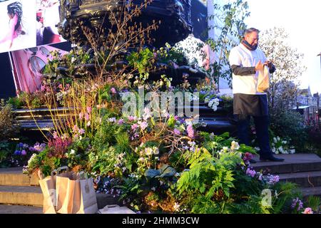 Pflanzen und Blumen bedecken den Shaftesbury Memorial Fountain, der oft als „Eros“ bekannt ist, im Piccadilly Circus, London, Großbritannien. Für einen Tag am 10th. Februar 2022 wurde damit eine Green Planet Augmented Reality Experience angekündigt, die am 11th. Februar 2022 im Piccadilly Circus eröffnet wurde. Partner und Unterstützer des Projekts sind BBC Earth, EE, Crown Estate, Factory 42, Kew Royal Botanic Gardens, Talesmith und Dimension. Das Projekt bietet die Online-Buchung von Freikarten an und läuft bis zum 9th. März 2022. Adam, ein Botschafter des Projekts, steht vor der Statue, bereit, die Passanten zu informieren. Stockfoto