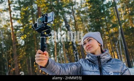 Frau, die auf einem Handheld-Film hält 3-Achsen-Gimbal-Stabilisiergerät im Winter für Smartphone. Girl Blogger Make Selfie, Broadcast Video Blogging, Vlogging. Videograf Operator Nimmt Fotovideo Auf. Stockfoto