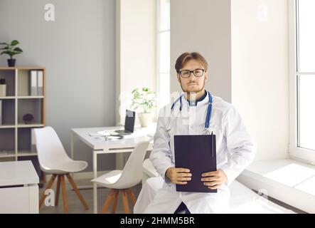 Porträt eines selbstbewussten jungen männlichen Arztes, der im Büro des modernen medizinischen Zentrums steht. Stockfoto