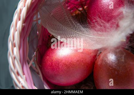 Bunt bemalte, glänzende Ostereier aus Marmor in einem Korb mit zarten Federn aus der Nähe. Nest mit Stroh - Osterdekoration auf dem Tisch Stockfoto