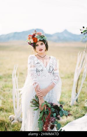 Braut in einem Kranz mit Strauß steht auf dem Rasen Stockfoto