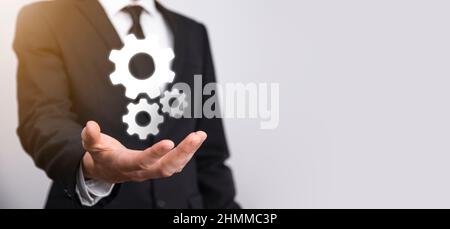 Geschäftsmann im Anzug hält Metallgetriebe und Zahnräder Mechanismus der Interaktion Teamarbeit Konzept, Hand halten Gruppe von virtuellen Zahnräder Rad. Stockfoto