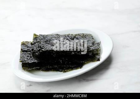 Asiatische Lebensmittel Laver, Gewürzte Laver, Sesamöl, Sesamsamen, Schwarzer Pfeffer. Auf Weißem Tisch Stockfoto
