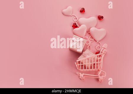 Herzförmige Ballone im rosa Warenkorb auf rosa Hintergrund. Saisonverkauf, Frühjahrsshopper-Konzept. Valentinstag. Stockfoto