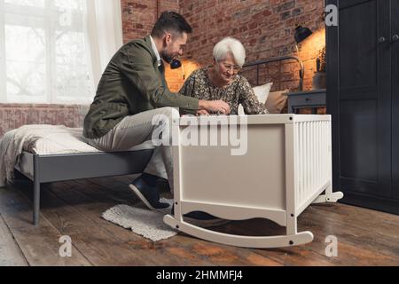 Die kaukasische Großmutter bekommt die Aufnahme ihres Sohnes mittleren Alters in der Halle mit ihrem neugeborenen Baby zu sehen. Hochwertige Fotos Stockfoto