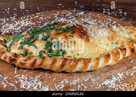 Pizza Calzone mit Speck und Käse, Kräutern und Kirschtomaten. Mit Mozzarella, Garnelen und Kraken, Muscheln und anderen Produkten auf einem Holzhinterholz Stockfoto