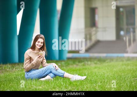 Ein junges Mädchen schreibt sms. Draußen auf dem Gras sitzen an einem Sommertag. Stockfoto