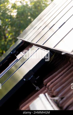 Nahaufnahme einer Installation einer Reihe von Sonnenkollektoren, die auf einem Haus mit Dachziegeln installiert sind. Stockfoto