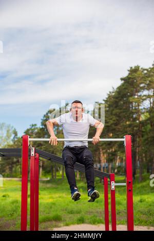 Der kaukasische Mann zieht sich auf einer horizontalen Stange auf einem Sportplatz hoch. Stockfoto