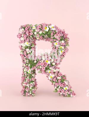 Kreatives Schreiben R Konzept aus frischen Frühling Hochzeitsblumen. Blumenschriftkonzept auf pastellrosa Hintergrund.