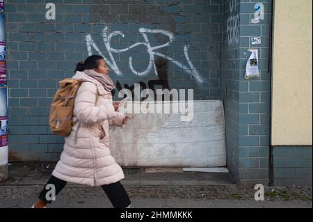 16.12.2021, Berlin, Deutschland, Europa - Eine Frau geht an einer alten, schmutzigen und illegal weggeworfenen Matratze vorbei, die an einer verschmierten Wand des Gebäudes lehnt. Stockfoto