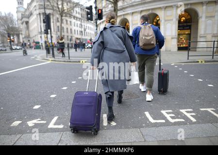 London, England, Großbritannien. Zwei Personen mit Gepäck überqueren die Straße am Trafalgar Square Stockfoto