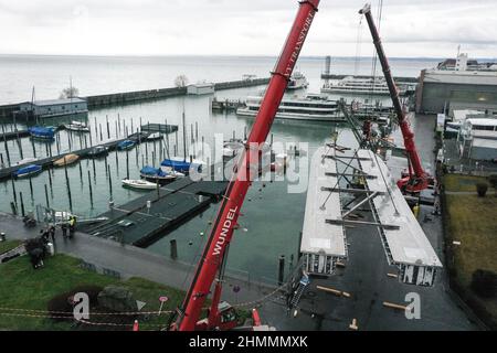 Friedrichshafen, Deutschland. 11th. Februar 2022. Zwei Krane heben die beiden Rümpfe für den zukünftigen E-Katamaran von Land in das Hafenbecken. Die Rümpfe wiegen rund 20 Tonnen und wurden in Stralsund gebaut. Am Morgen kamen die Rümpfe von der Werft mit einem Schwerlasttransporter in Friedrichshafen an. Quelle: Felix Kästle/dpa/Alamy Live News Stockfoto