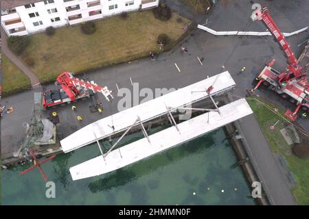 Friedrichshafen, Deutschland. 11th. Februar 2022. Zwei Krane heben die beiden Rümpfe für den zukünftigen E-Katamaran von Land in das Hafenbecken. (Luftaufnahme mit einer Drohne) die Rümpfe wiegen rund 20 Tonnen und wurden in Stralsund gebaut. Am Morgen kamen die Rümpfe von der Werft mit einem Schwerlasttransporter in Friedrichshafen an. Quelle: Felix Kästle/dpa/Alamy Live News Stockfoto