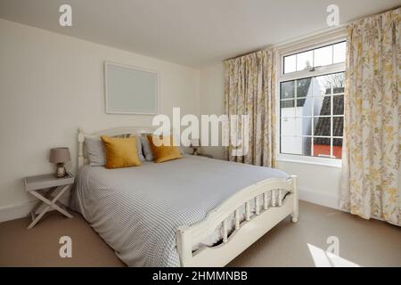 Hemingford Gray, Cambridgeshire - Feb 10 2018: Möbliertes Schlafzimmer mit karierter Bettdecke und orangefarbenen Kissen mit Sonnenschein durch das Fenster. Stockfoto