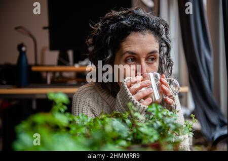 Nijmegen, Niederlande. 10th. Februar 2022. Eine Frau wird dabei gesehen, wie sie eine Tasse Kaffee in einem warmen Pullover trägt.der Warm Sweater Day wird jedes Jahr an einem Freitag im Februar vom Klimaatverbond Nederland (Climate Association Netherlands) organisiert, einem Zusammenschluss öffentlicher Organisationen mit Ambitionen im Bereich Nachhaltigkeit und Klimawandel. Es handelt sich um eine nationale Klimaschutzmaßnahme, bei der alle Teilnehmer versprechen, die Heizung in ihren Häusern, Büros, am Arbeitsplatz oder in ihren Klassenzimmern zu senken. Statt den Raum zu erhitzen, heizen sie sich selbst auf, indem sie ein bequemes, Stockfoto