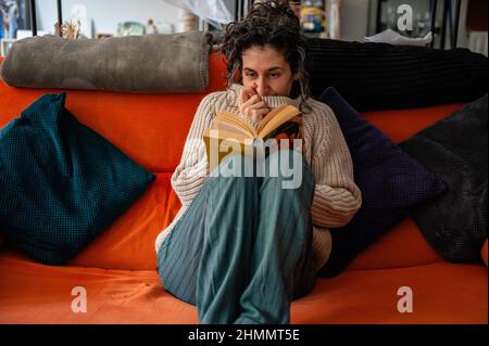 Nijmegen, Niederlande. 10th. Februar 2022. Eine Frau sitzt zu Hause auf ihrer Couch, während sie einen warmen Pullover trägt, nachdem sie die Heizung heruntergedreht hat.der Warm Sweater Day wird jedes Jahr an einem Freitag im Februar vom Klimaatverbond Nederland (Climate Association Netherlands) organisiert. Das ist ein Zusammenschluss öffentlicher Organisationen mit Ambitionen im Bereich Nachhaltigkeit und Klimawandel. Es handelt sich um eine nationale Klimaschutzmaßnahme, bei der alle Teilnehmer versprechen, die Heizung in ihren Häusern, Büros, am Arbeitsplatz oder in ihren Klassenzimmern zu senken. Anstatt den Raum aufzuheizen, sie er Stockfoto