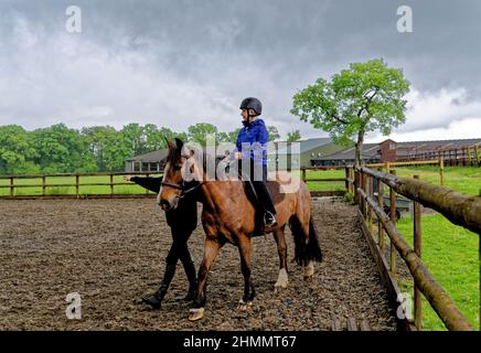 Mädchen mit ihrem ersten Reitunterricht bareback mit Helm und Ausbilder. Wellington Riding School, Hook, Vereinigtes Königreich. 11.05.2016 Stockfoto